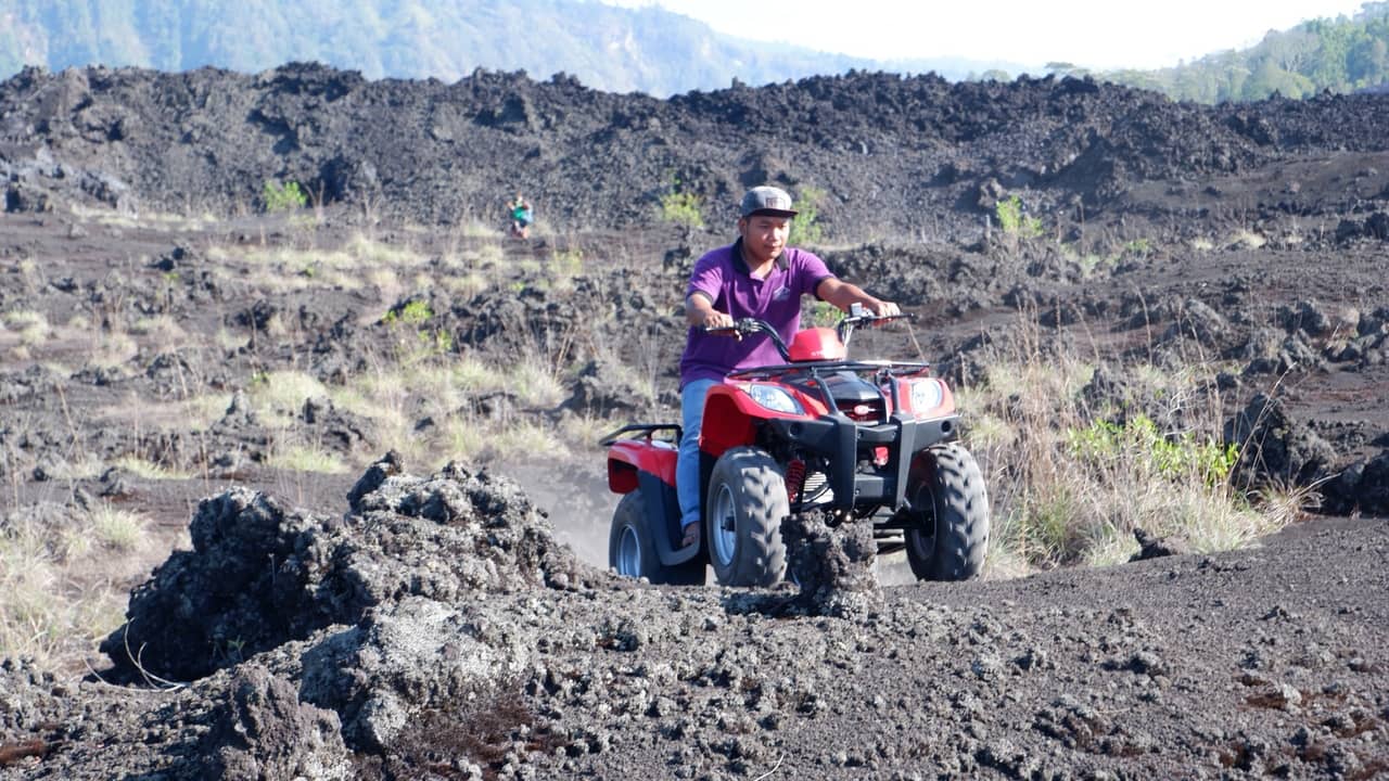 A man in a purple shirt rides a red quad bike across Mount Batur’s dark volcanic terrain.