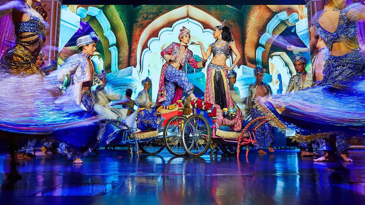 Performers in colorful costumes on a stage with a digital palace backdrop at Simon Cabaret Show in Phuket