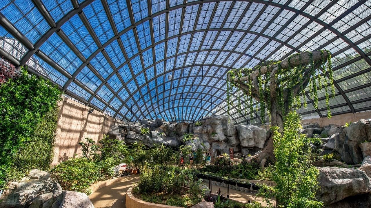 Visitors walking through a curved-glass conservatory with rocky formations and lush greenery at Entopia by Penang Butterfly Farm