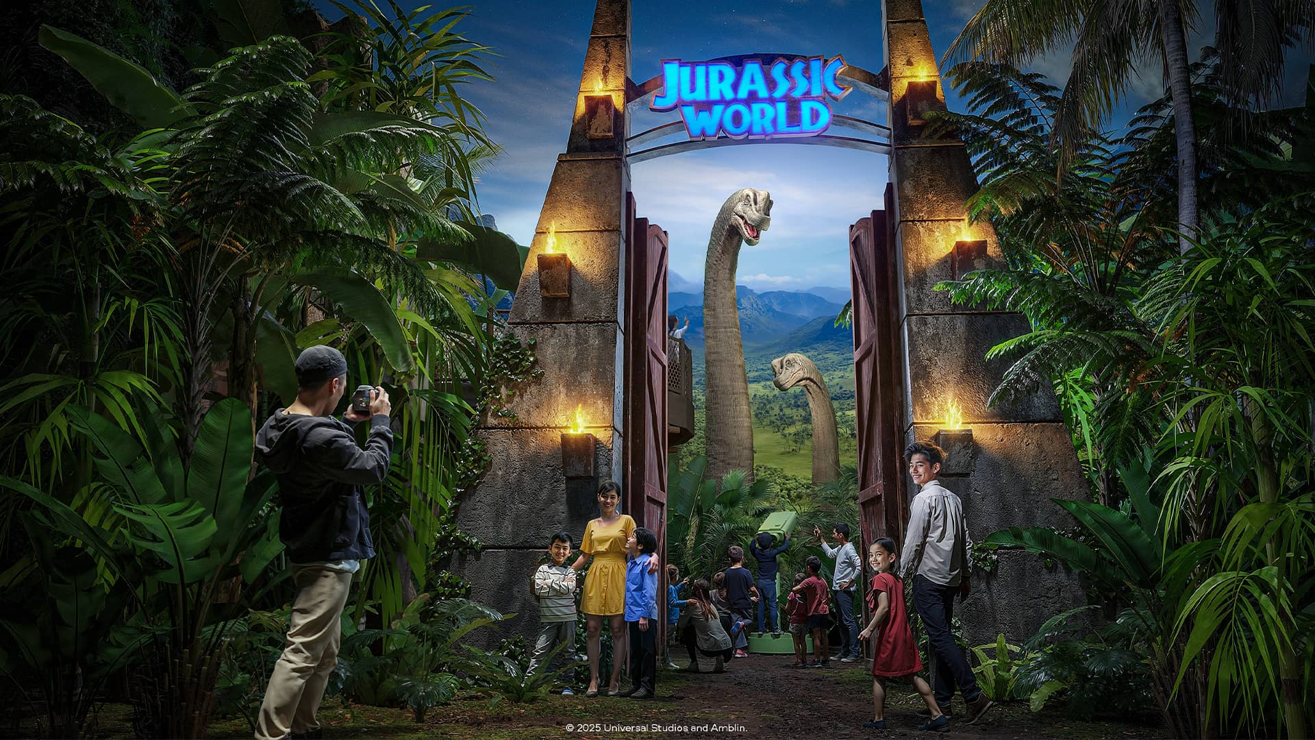 Visitors walk beneath a stone Jurassic World gate into a lush tropical landscape with long-necked dinosaurs ahead.